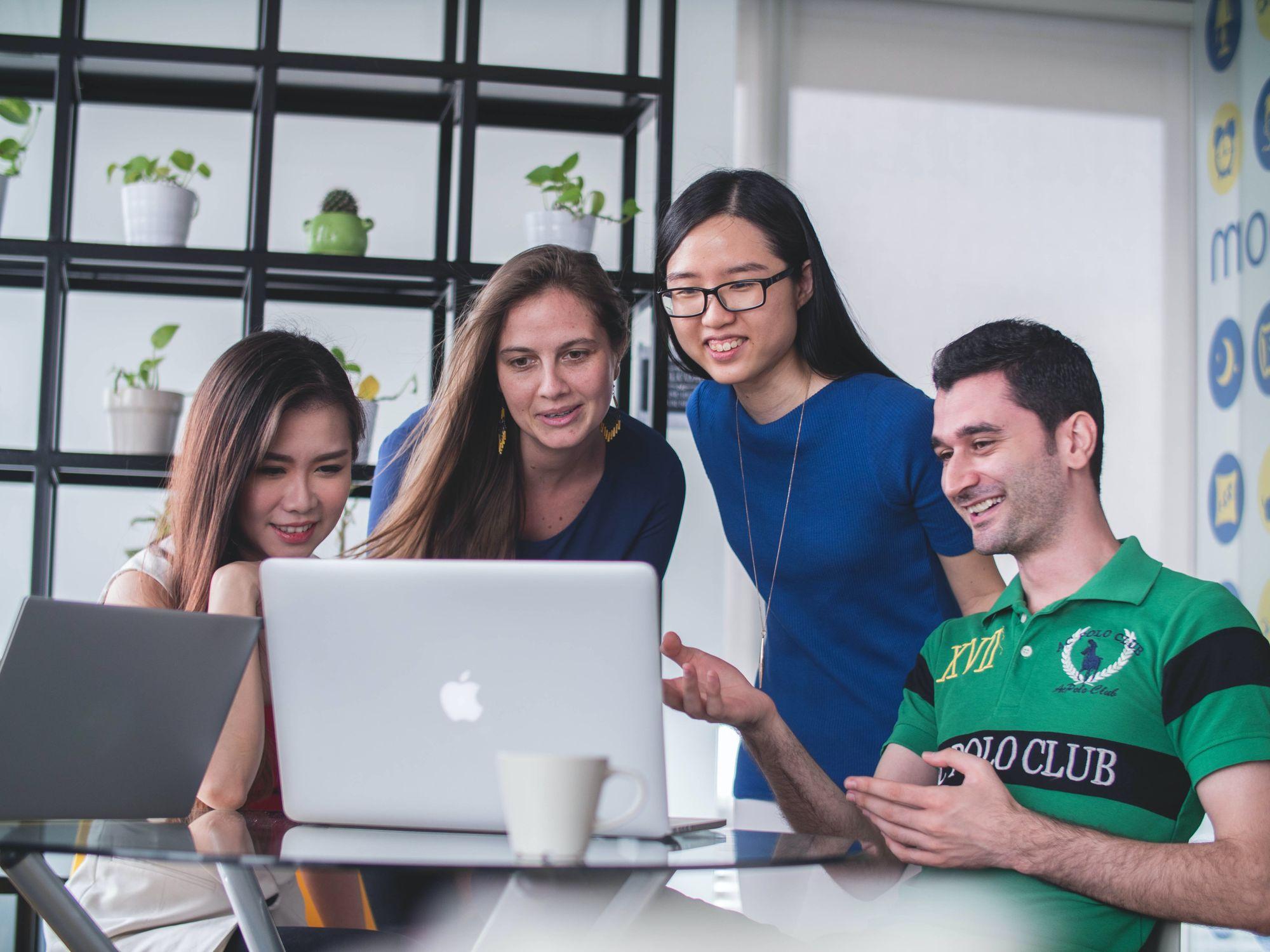 a group of four friends crowd around a computer screen