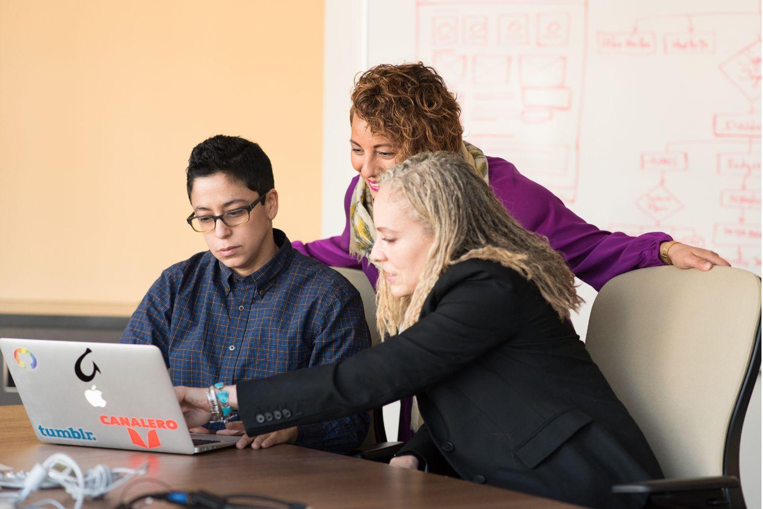 three colleagues gather around a laptop