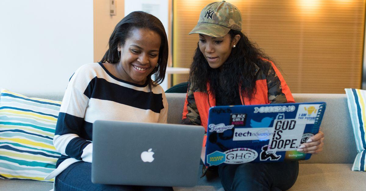 two women sit on a couch collaboratively pair programming